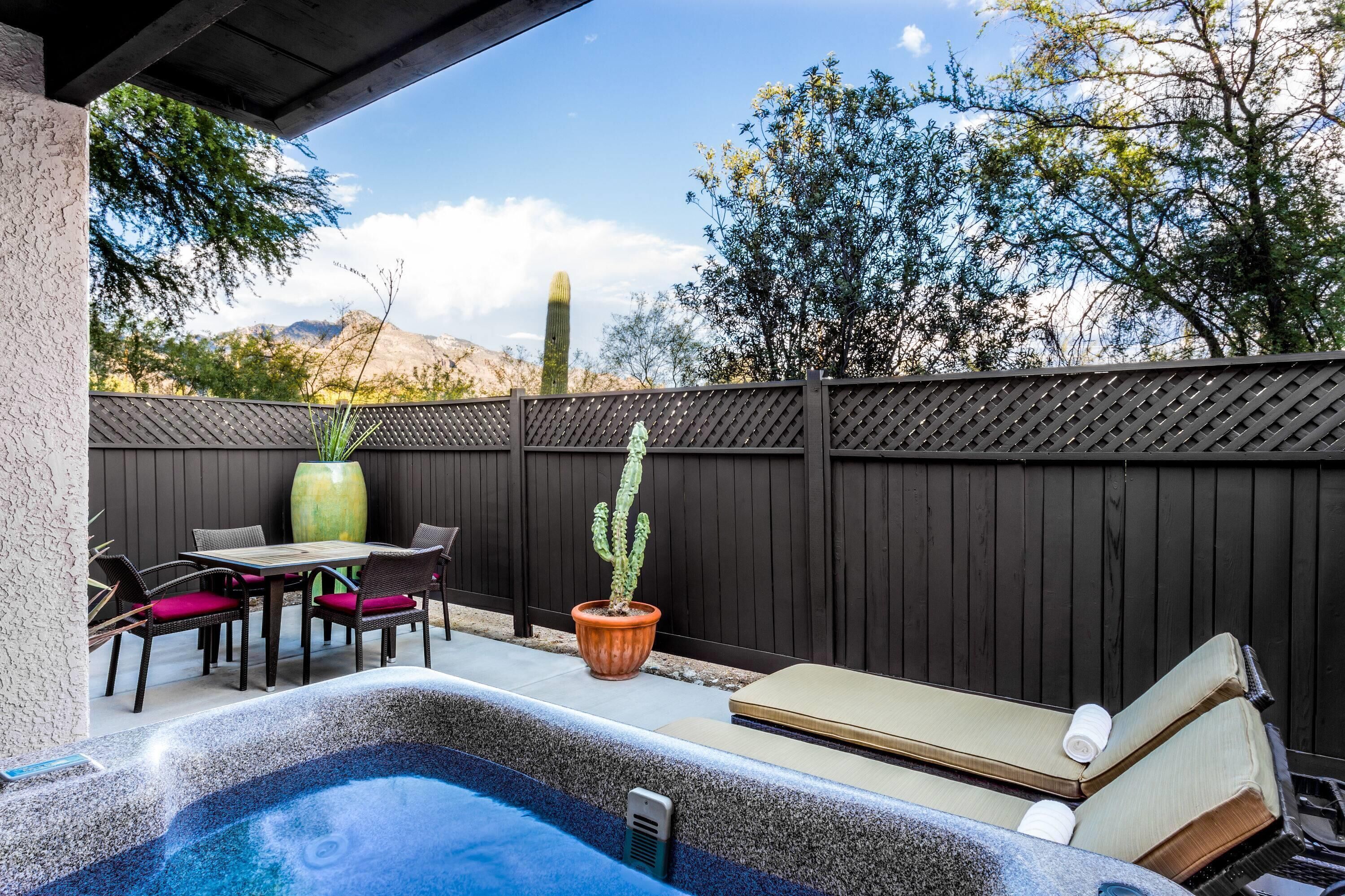 A hot tub with a wooden deck, a table with chairs, and a cactus plant.