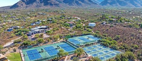 An aerial view of a residential area with multiple tennis courts surrounded by sparse vegetation and houses.
