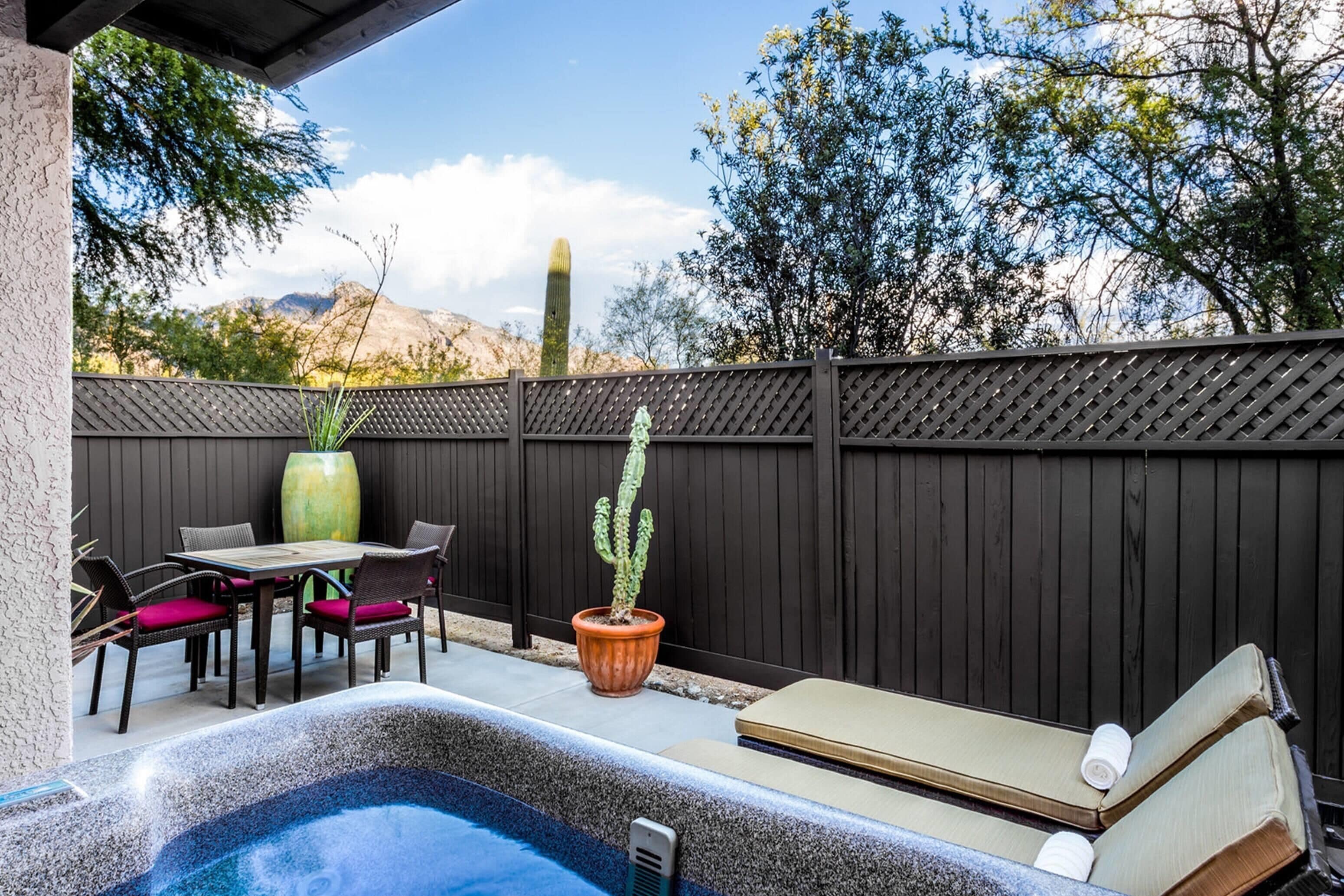 A hot tub with a wooden deck, a table with chairs, and a cactus plant.