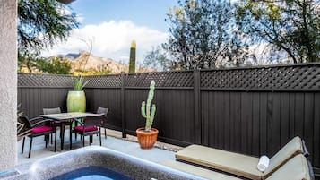 A hot tub with a wooden deck, a table with chairs, and a cactus plant.