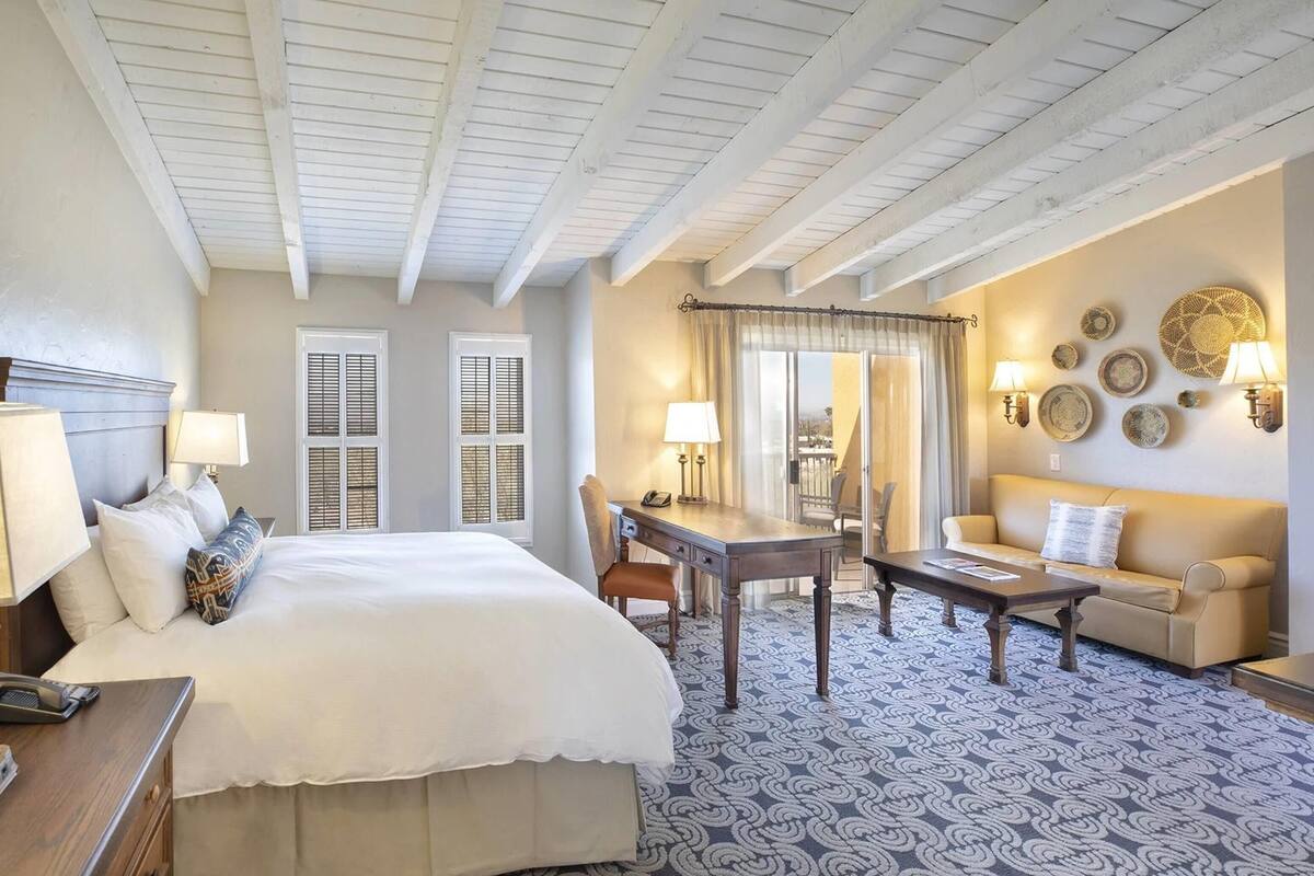 A hotel room with a bed, desk, chair, sofa, and a patterned carpet.