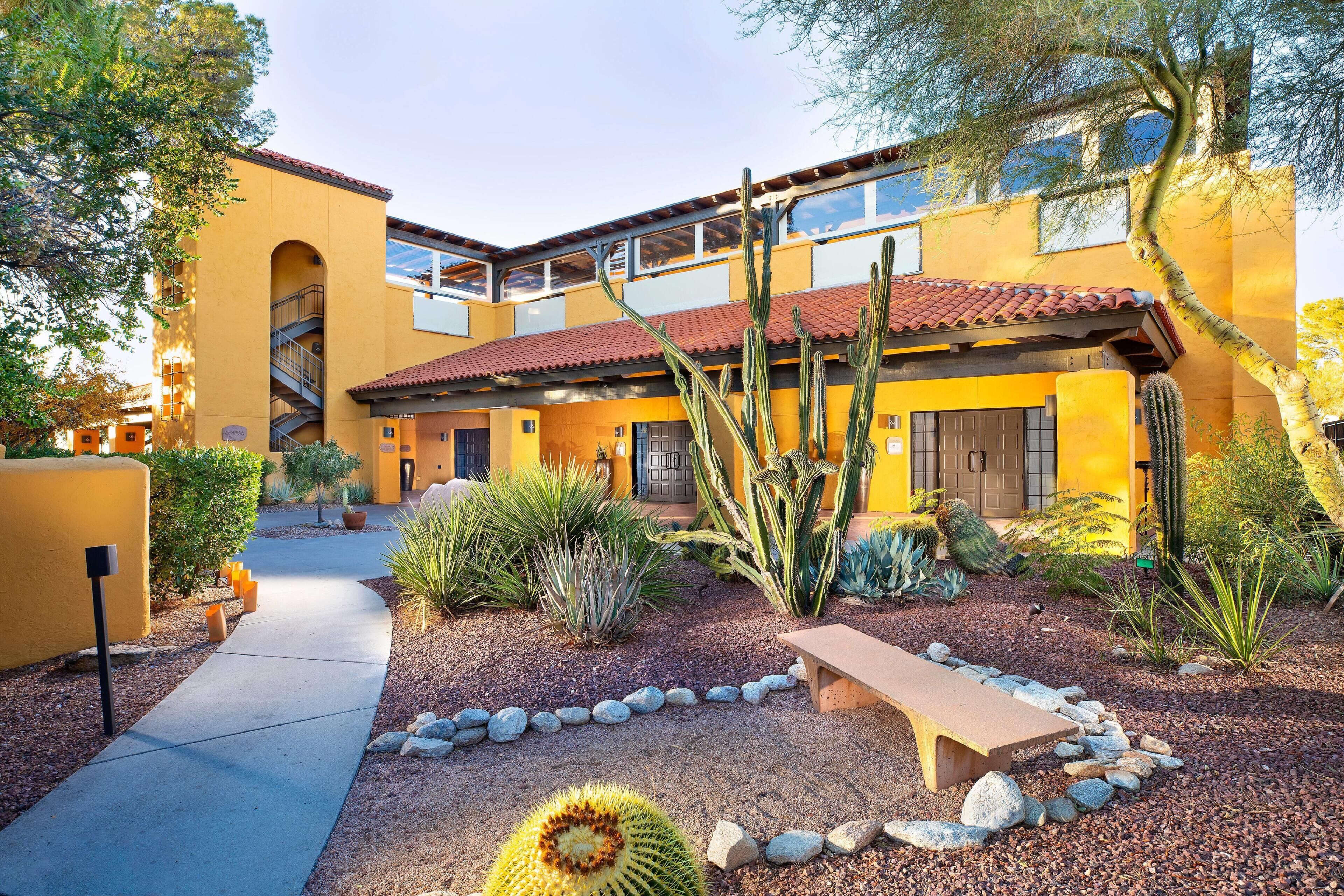 A building with a yellow facade, a red-tiled roof, and a cactus garden.