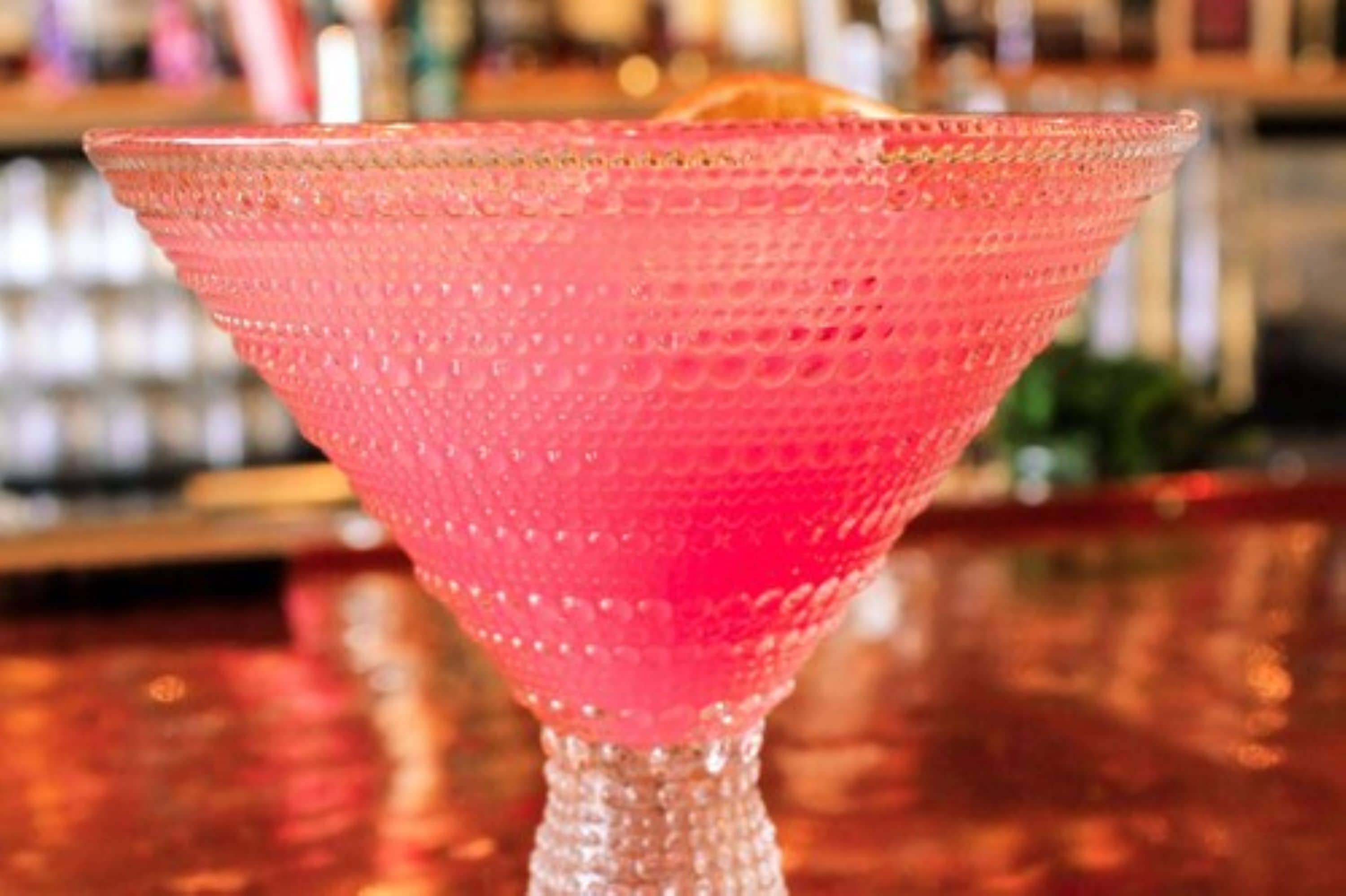 A pink textured cocktail glass on a bar counter.