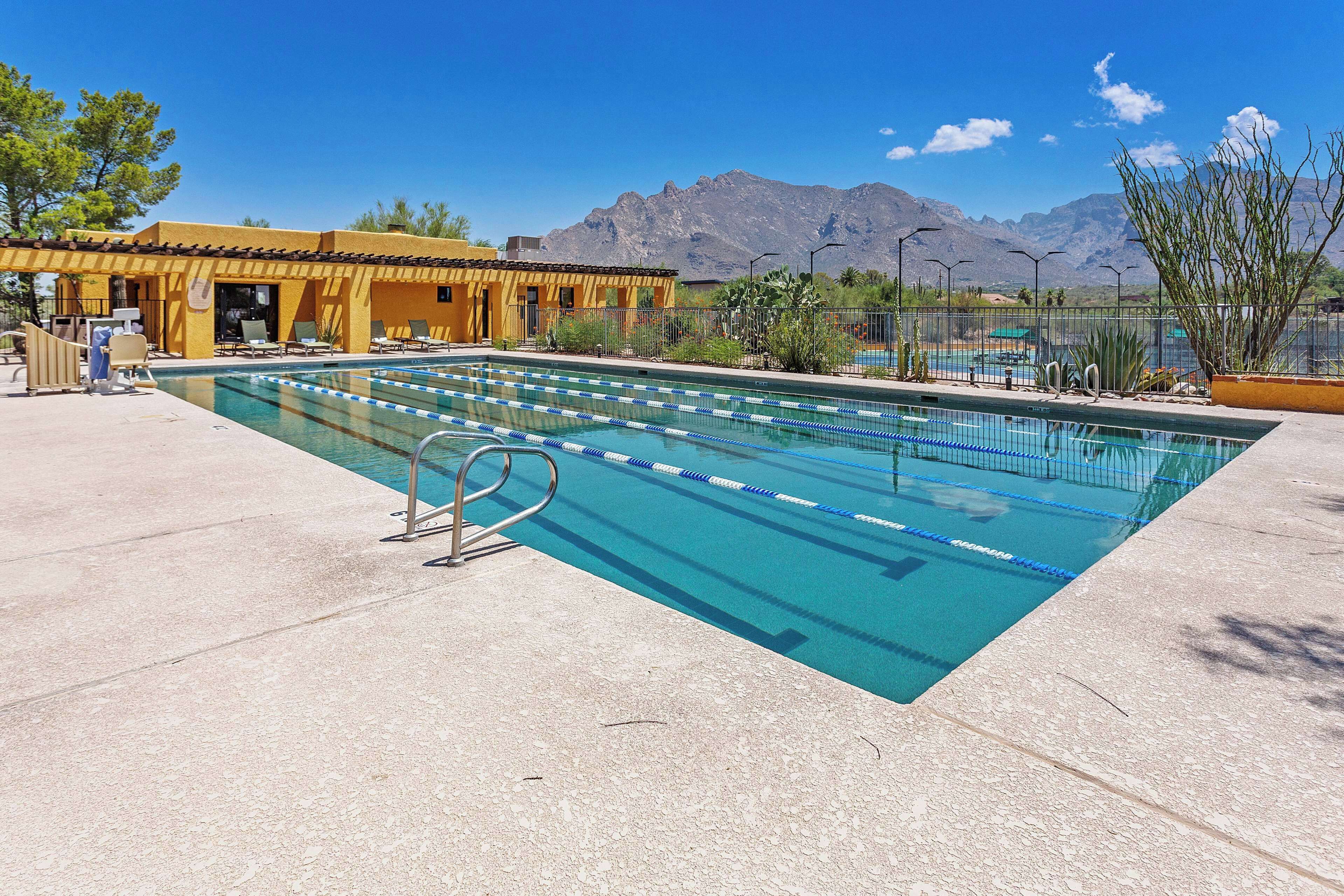 Ein Schwimmbecken mit klarem, blauen Wasser, ein Rettungsschwimmerstuhl und im Hintergrund ein Gebäude mit gelber Fassade.