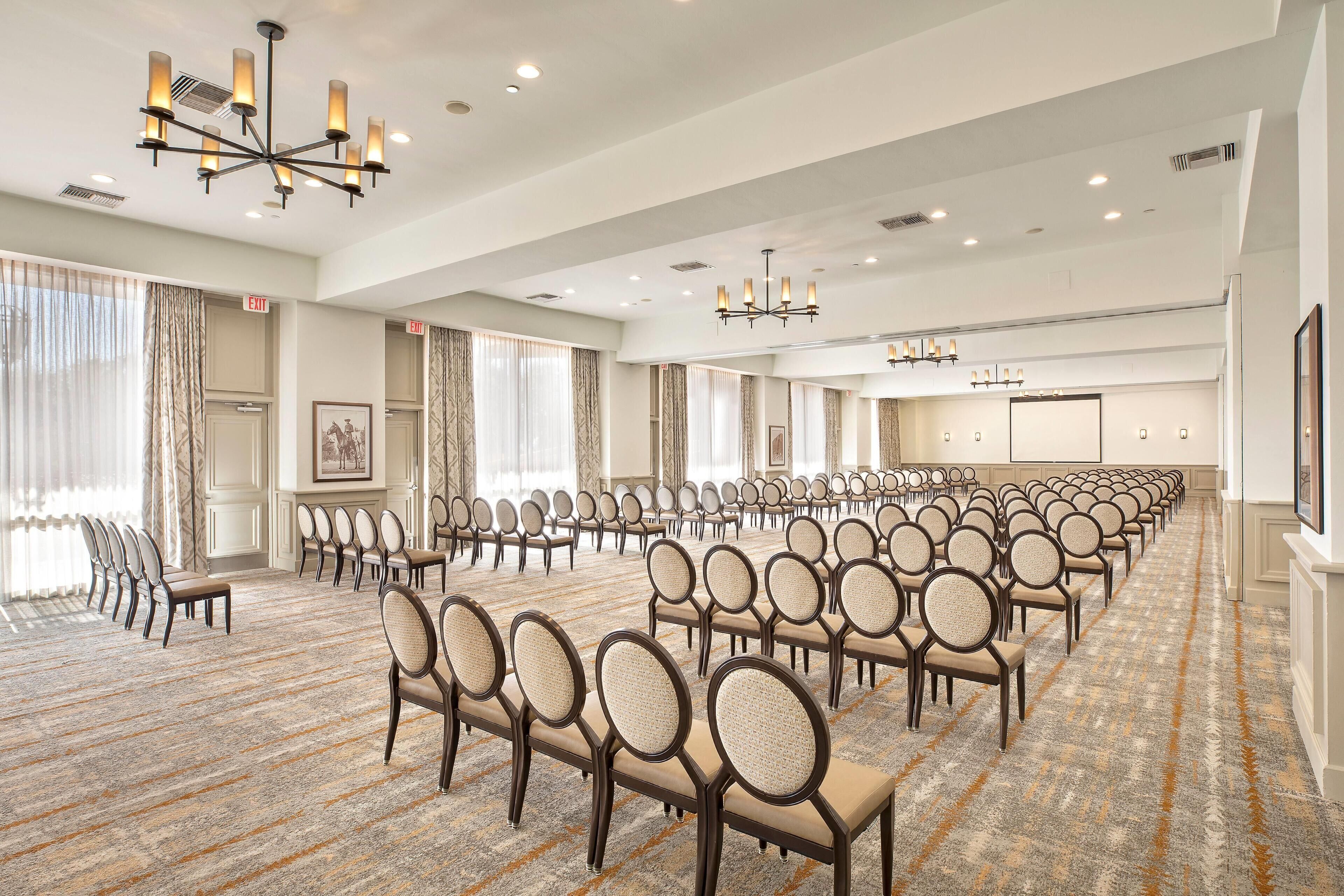 A conference room with rows of chairs, a projector screen, and a large window with curtains.