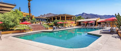 A pool area with lounge chairs, red umbrellas, and a mountain backdrop.