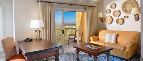 A room with a wooden table, a sofa, a patterned carpet, and a balcony with a view.