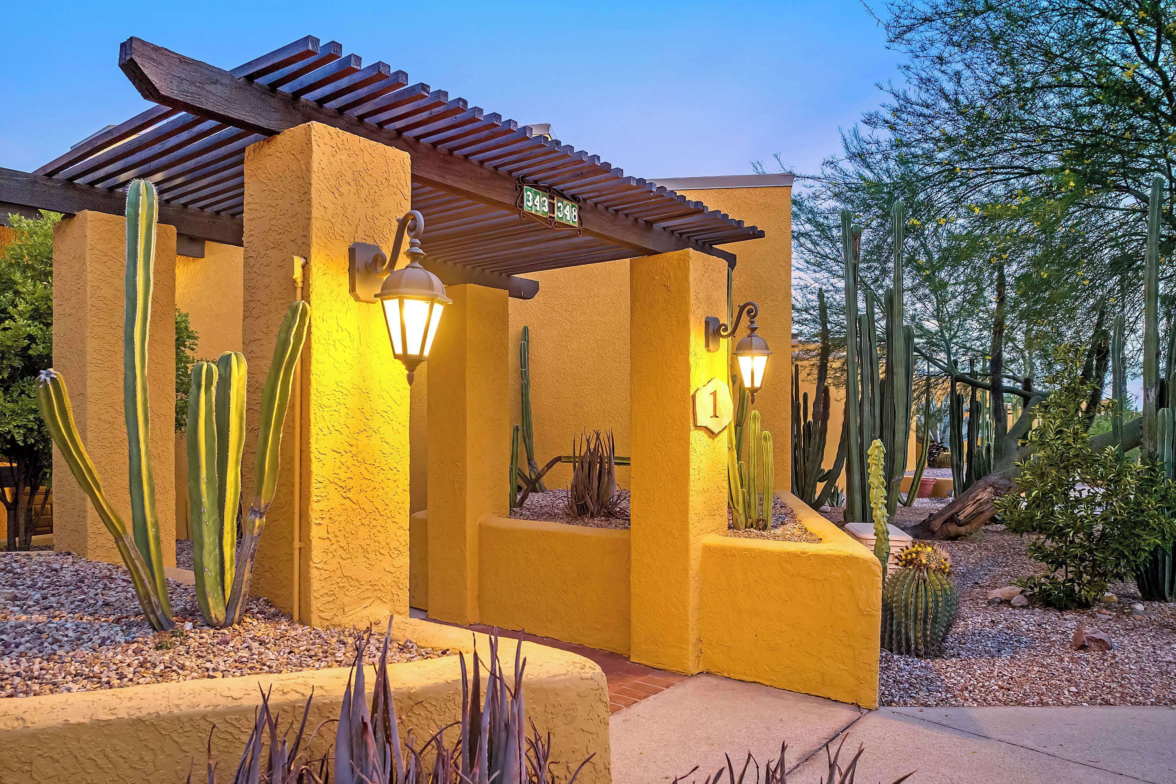 Un bâtiment à la façade jaune, agrémenté d’une pergola en bois et de quelques cactus.
