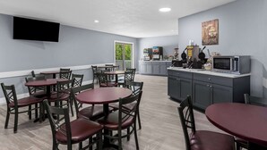 Una cocina moderna con microondas, tostadora y cafetera. Hay varias mesas y sillas para comer.