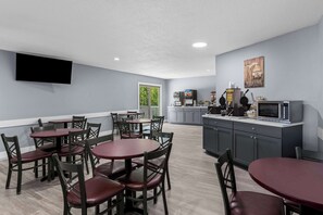 A modern kitchen with a microwave, toaster, and coffee maker. There are multiple dining tables and chairs.