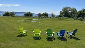 Un espacio verde con cinco sillas Adirondack mirando hacia un cuerpo de agua y colinas lejanas.