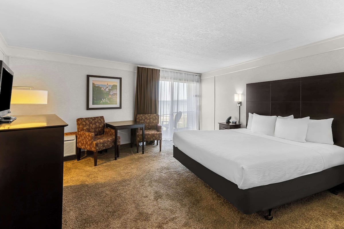A hotel room with a large bed, a desk with a chair, a television, and a painting on the wall.