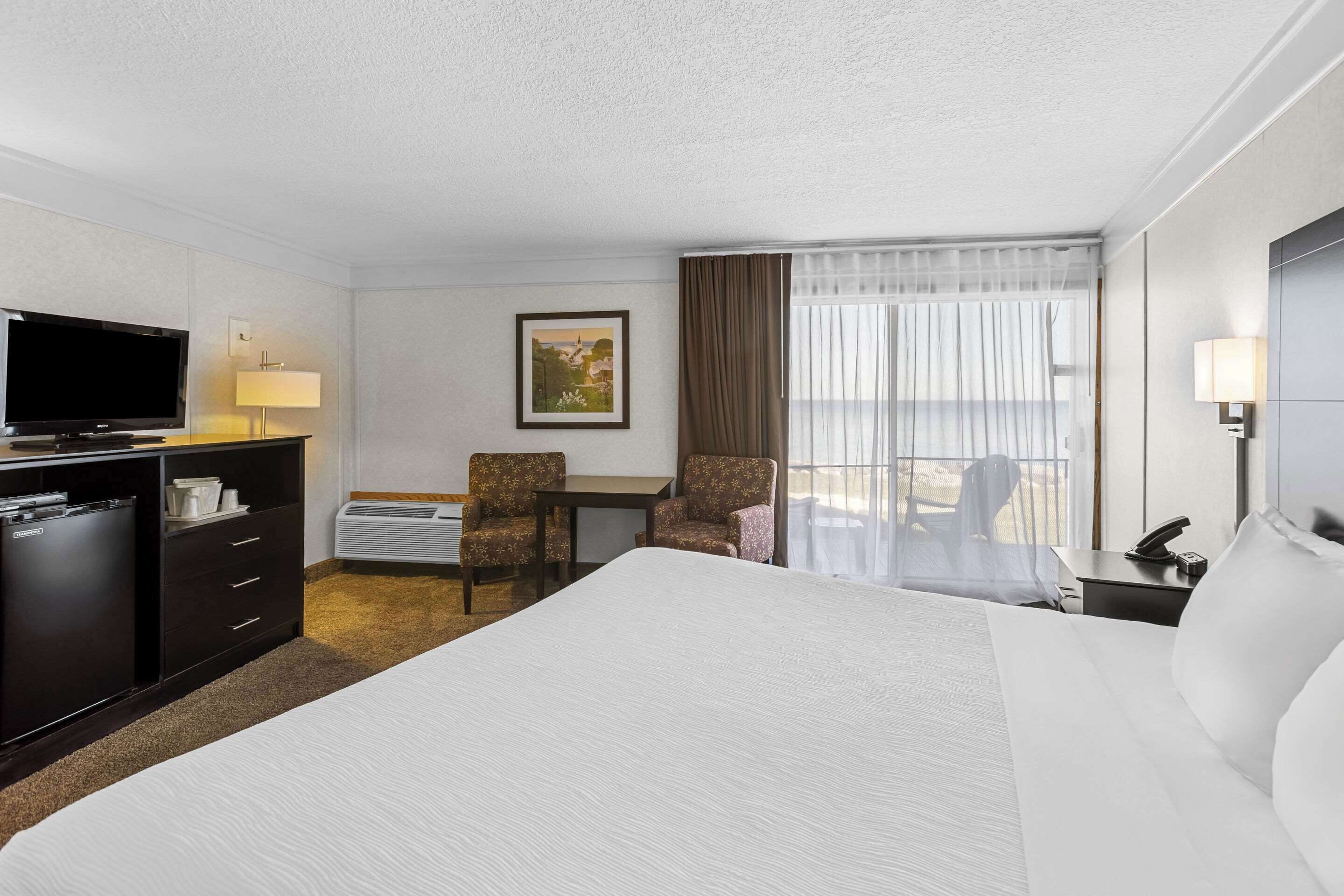 Habitación de hotel con una cama grande, un escritorio, un televisor, una silla y una ventana con cortinas.