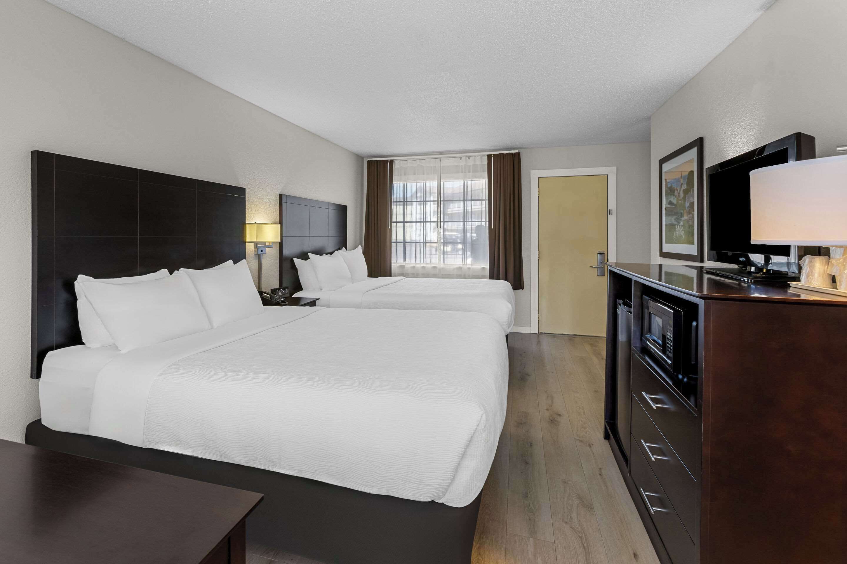 A hotel room with two beds, a TV, a desk, and a dresser.