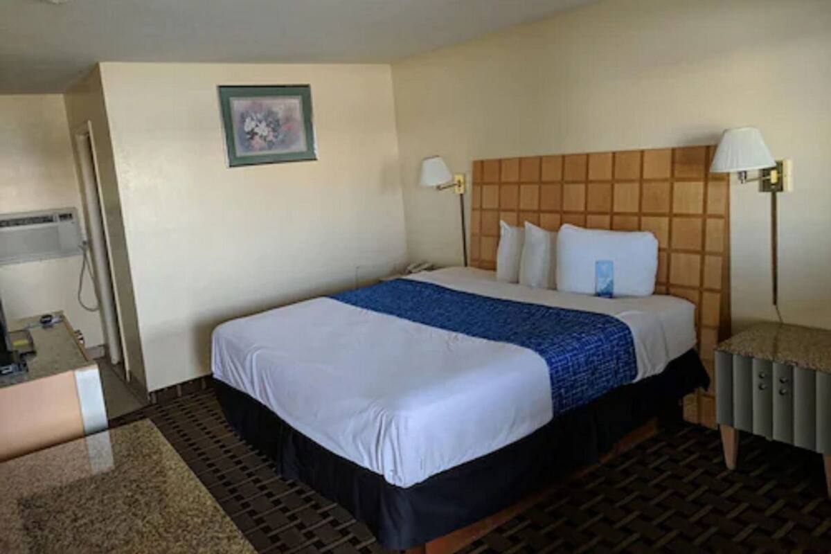 Habitación de hotel con cama, lámparas de noche, cabecero, una mesita y un cuadro en la pared.