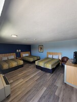 A hotel room with three beds, a desk, a chair, and a ceiling light.
