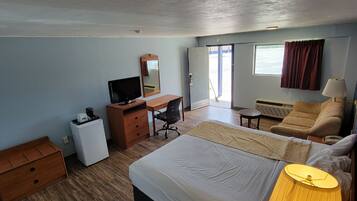 Habitación de hotel con cama, escritorio con silla, una mesita, sofá, televisor, espejo y ventana con cortinas.