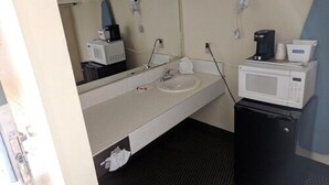 Une petite salle de bain avec un lavabo, un miroir et un four à micro-ondes posé sur un petit meuble.