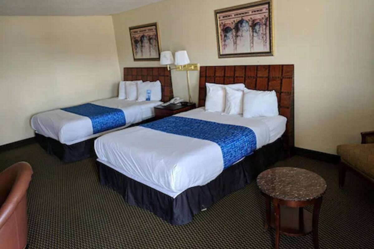 Una habitación de hotel con dos camas, una mesita redonda pequeña, una silla y una lámpara.