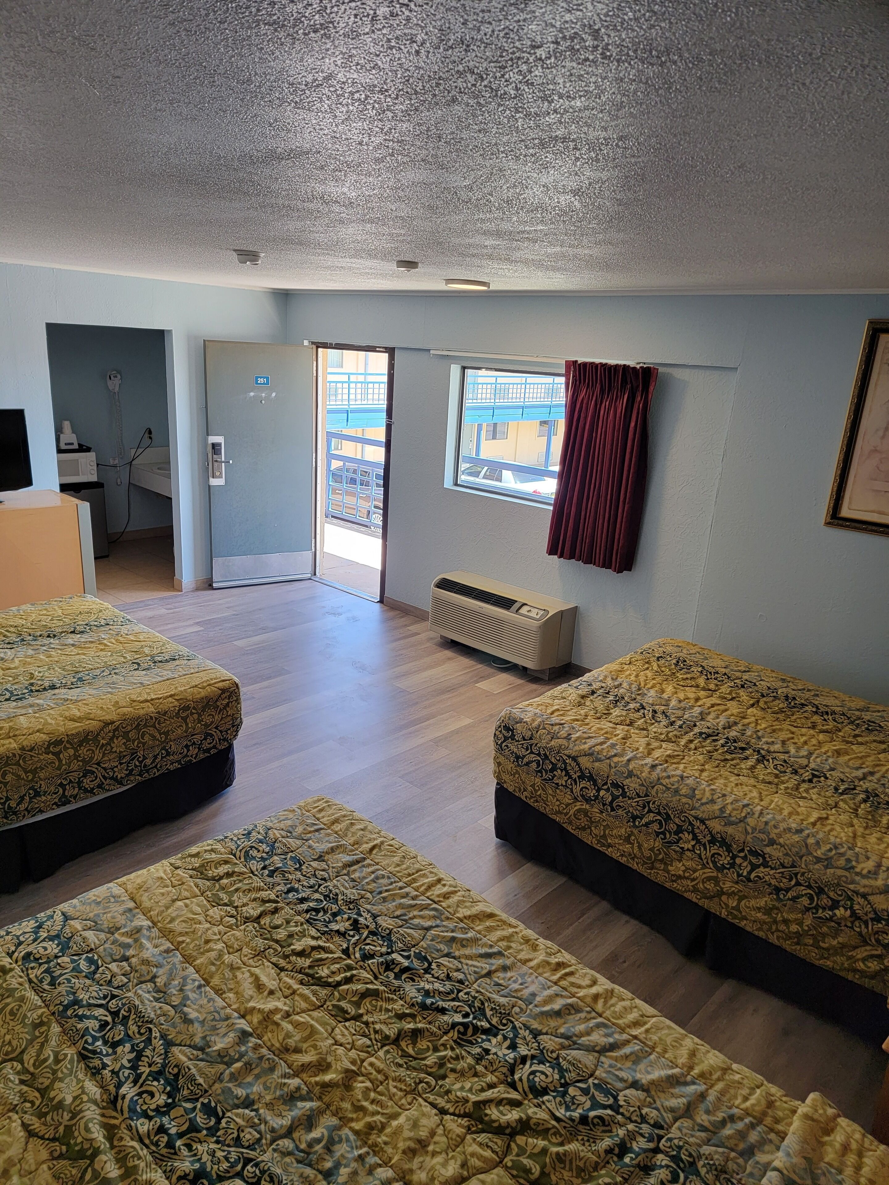 Habitación de hotel con dos camas, una ventana que da a un edificio, una puerta a un baño y un techo con una cámara de seguridad.