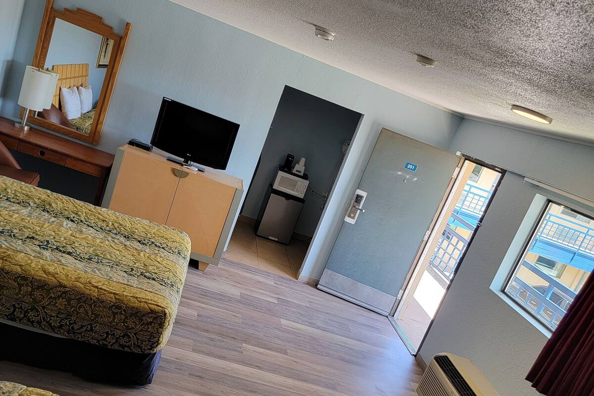 Una habitación de hotel con cama, escritorio, televisión, microondas y puerta que da a un balcón.