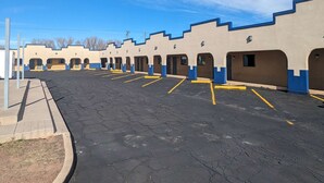 Une rangée de chambres de motel aux accents bleus et un parking avec des places délimitées.