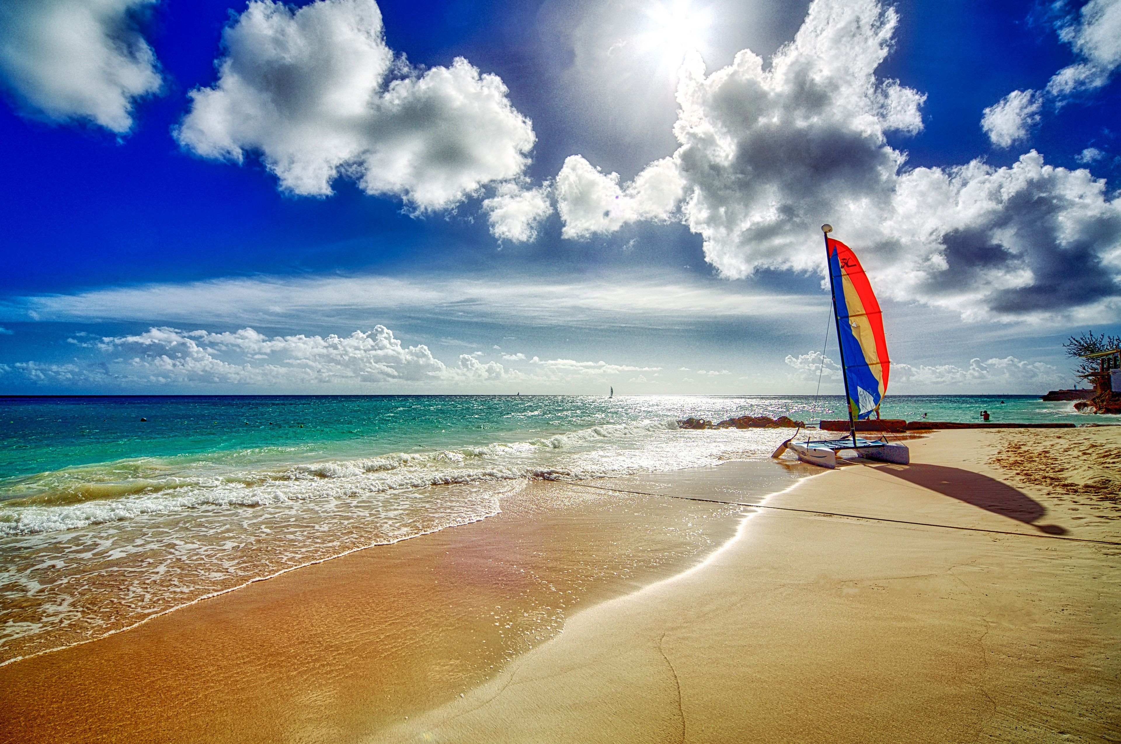 A beach with a sailboat, clear sky, and calm sea.