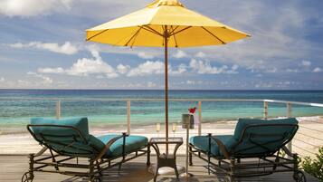 A deck with two lounge chairs and a table, a yellow umbrella, and a view of the ocean.