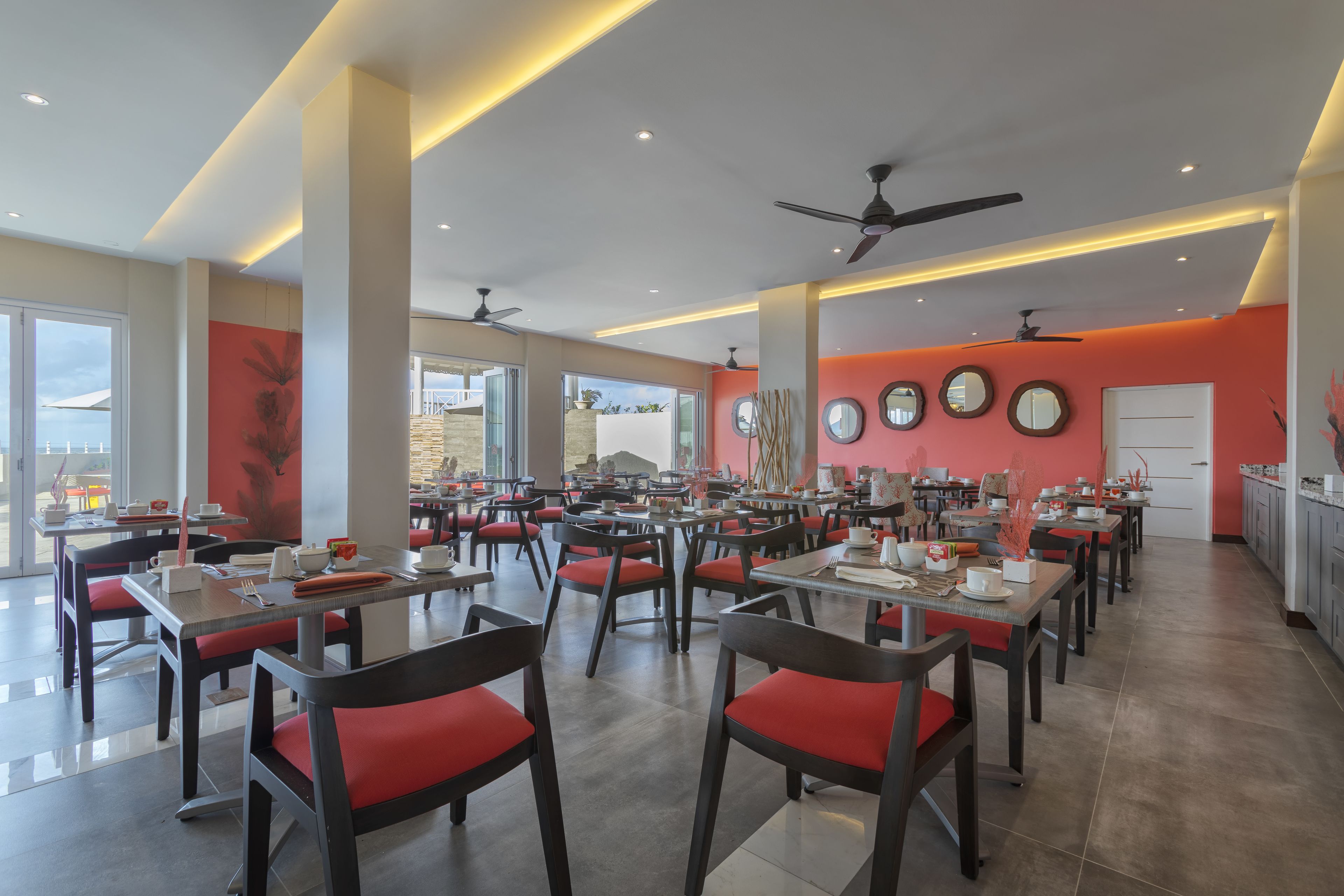 A spacious dining area with multiple tables and chairs, large windows, and ceiling fans.