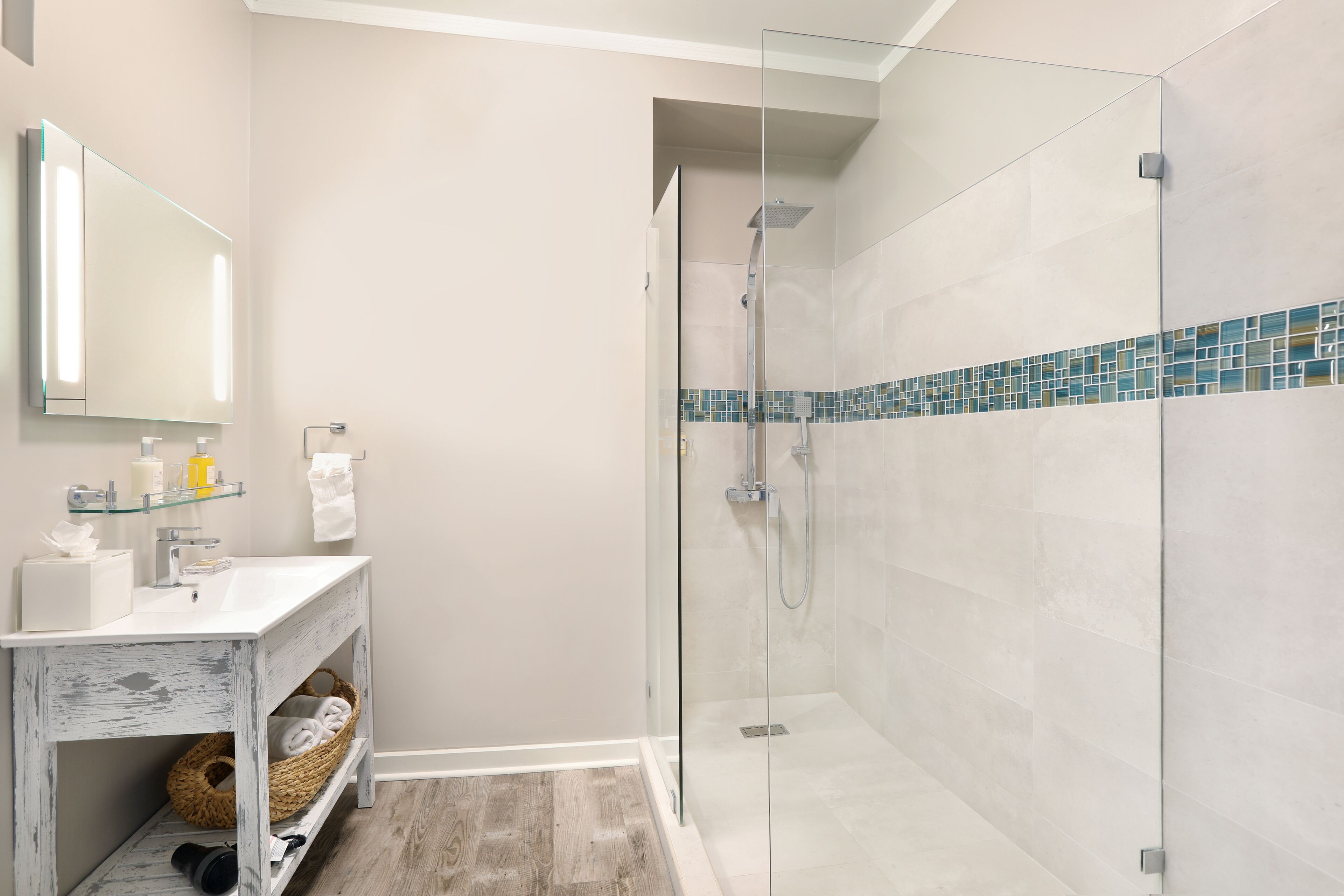 Un baño moderno con cabina de ducha de vidrio, un lavabo blanco con repisa de vidrio y un espejo sobre el lavabo.