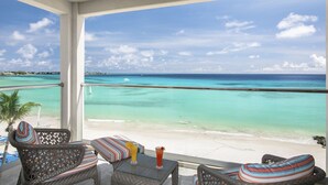 Un balcon agrémenté de meubles en osier, d’une table en verre et offrant une vue sur une mer turquoise et un ciel dégagé.