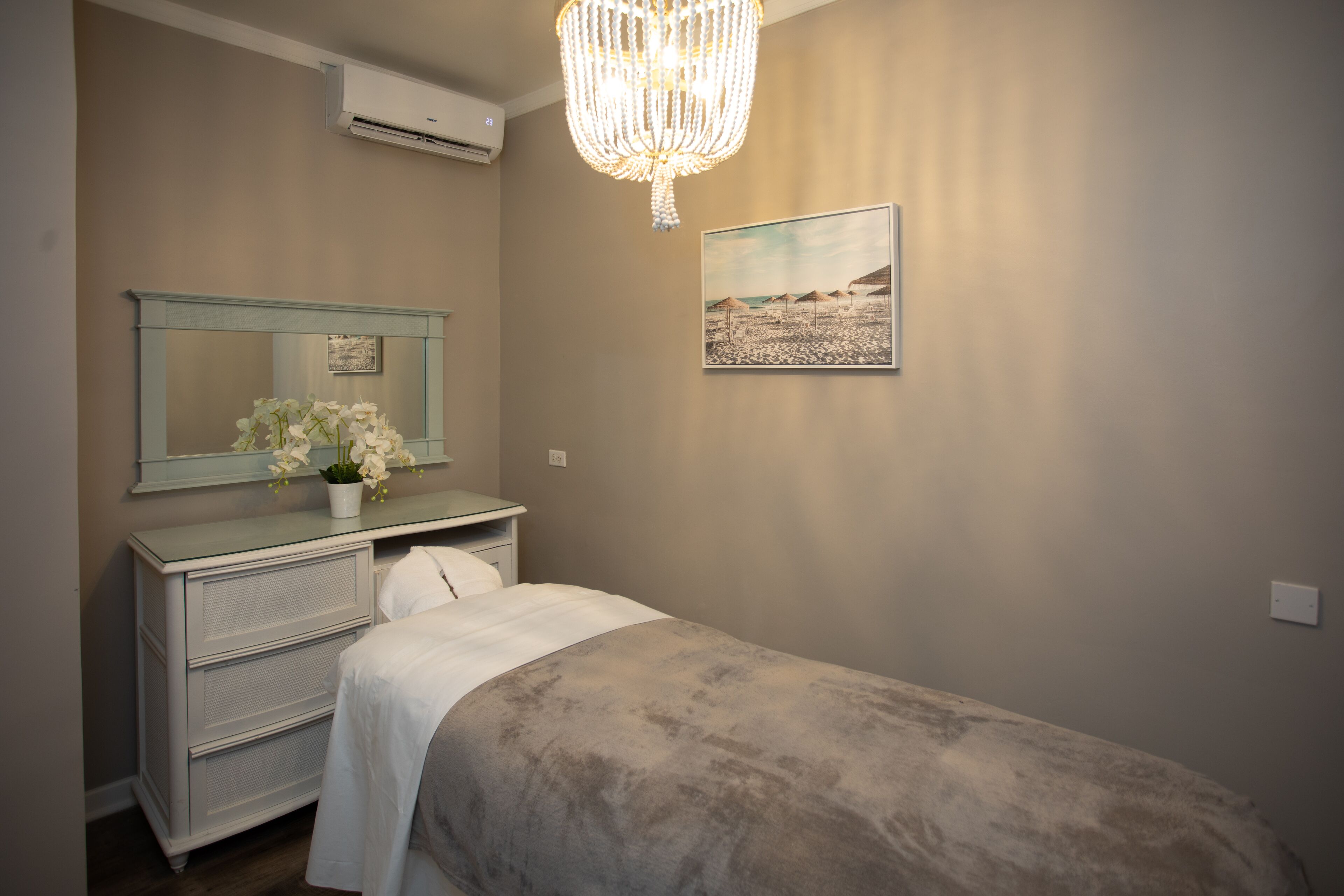 A bedroom with a bed, a dresser, a mirror, a chandelier, and a painting on the wall.
