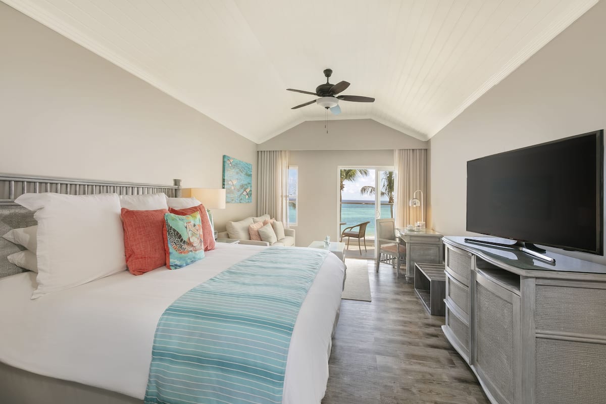 Une chambre d’hôtel avec un grand lit, une télévision, un ventilateur de plafond et une vue sur l’océan.