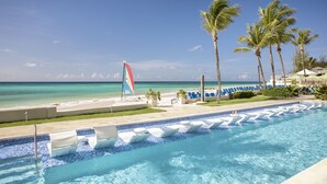 Une piscine avec des chaises longues et un voilier sur la plage.