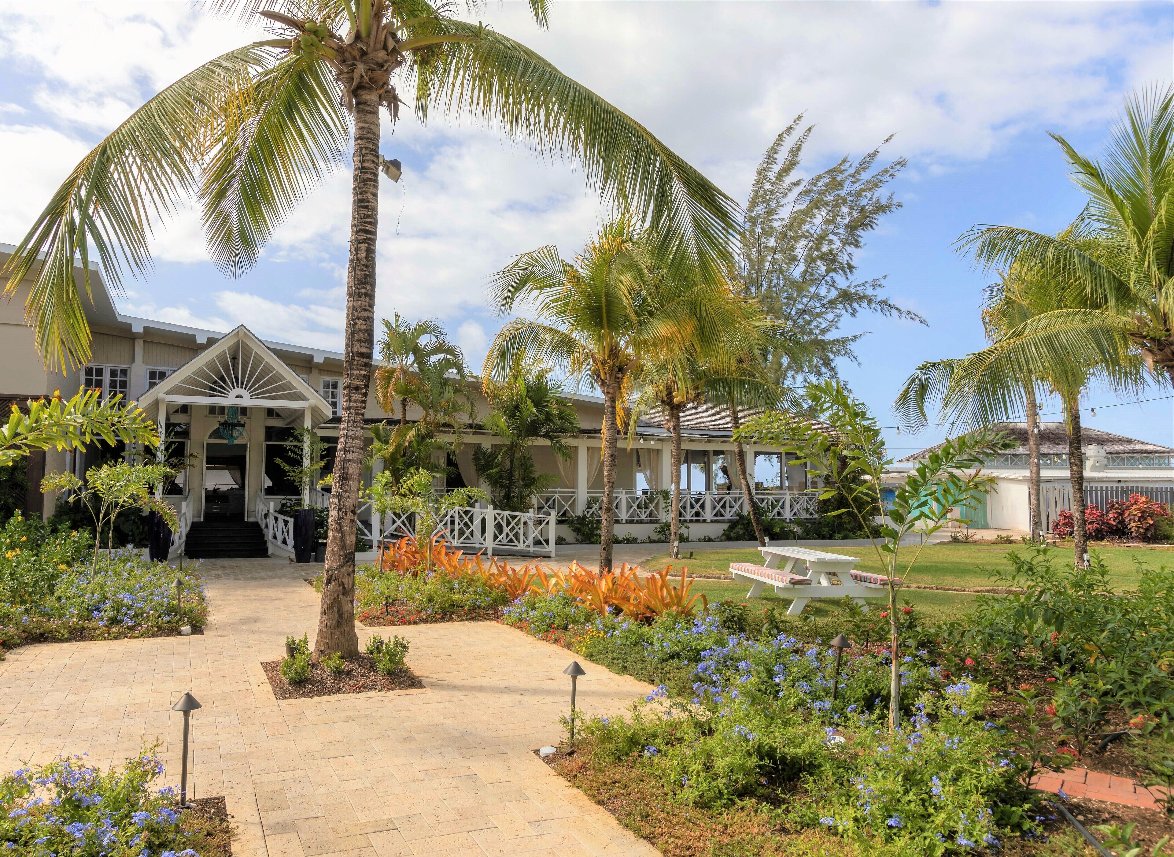 A resort with a covered walkway, palm trees, and a variety of flowering plants.