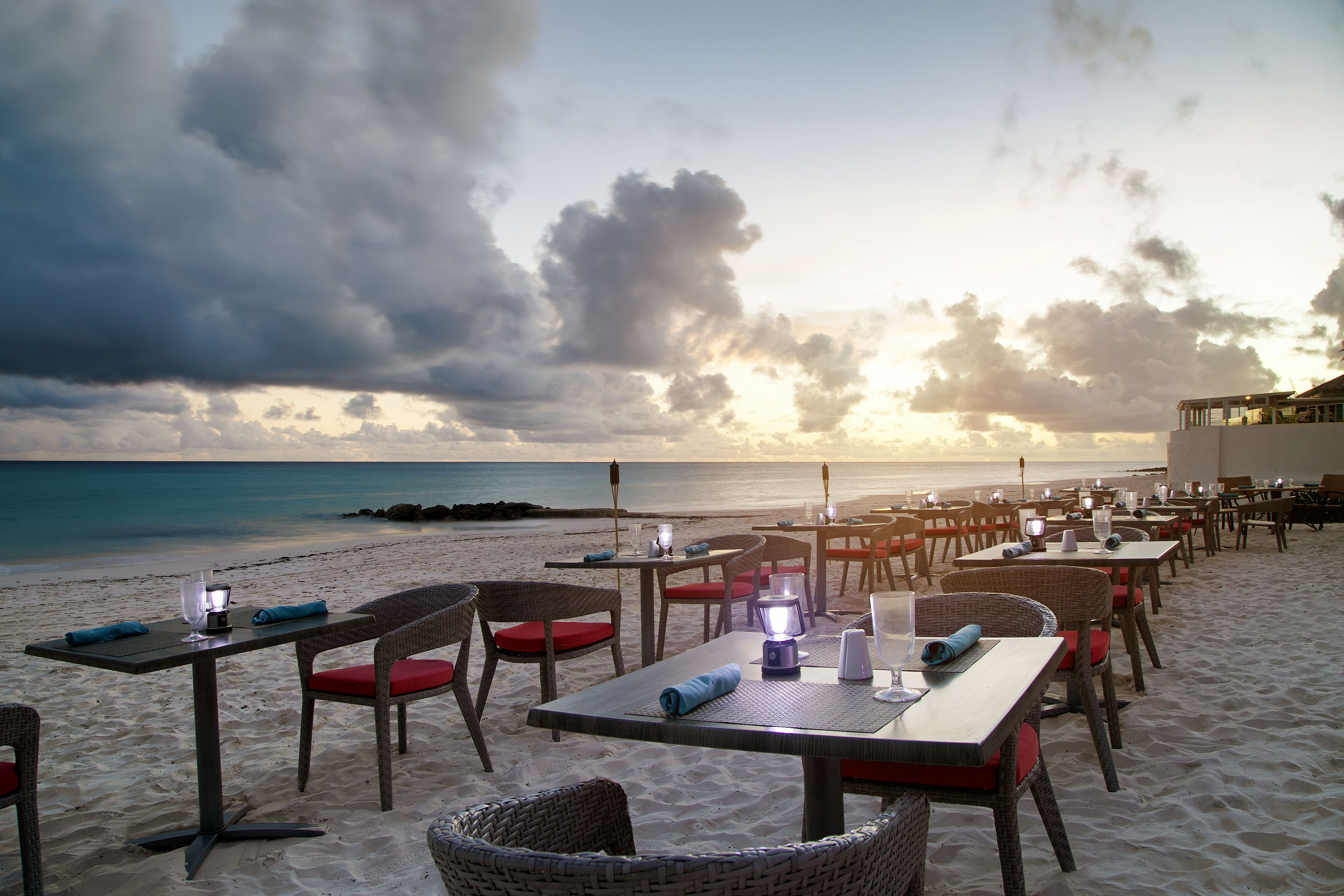 A beachside restaurant with tables and chairs, overlooking the ocean.