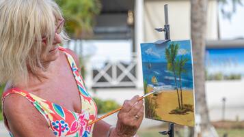 A person painting a landscape with palm trees and a sailboat.
