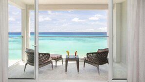 Un balcon agrémenté de meubles en osier et d’une table en verre, offrant une vue sur une mer turquoise et un ciel dégagé.