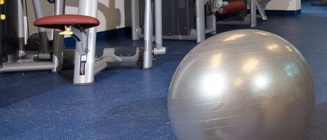 Un gimnasio con equipo de ejercicio, una pelota grande para ejercicio y mancuernas sobre un piso azul.