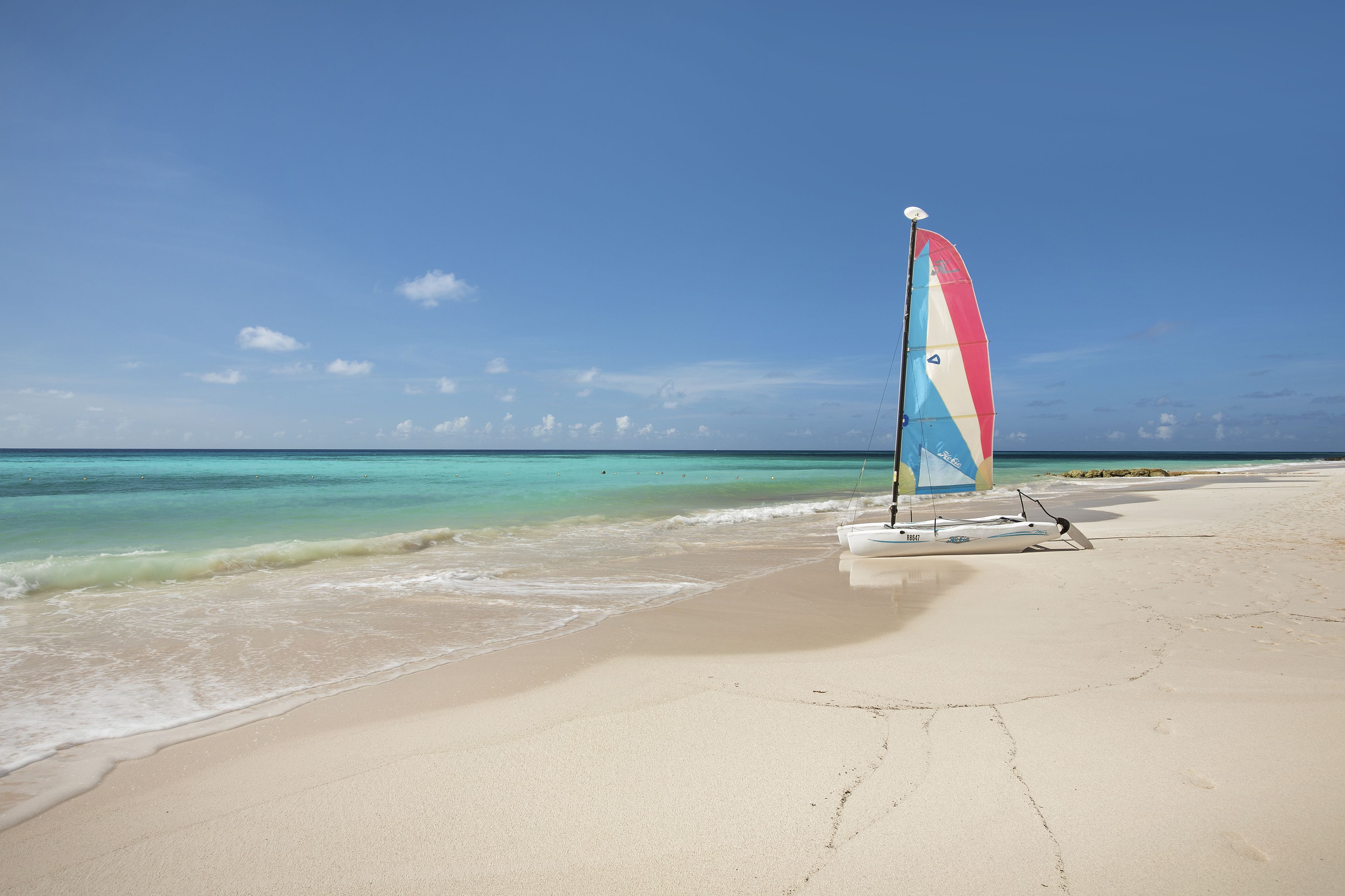 Una playa con un velero y aguas tranquilas.