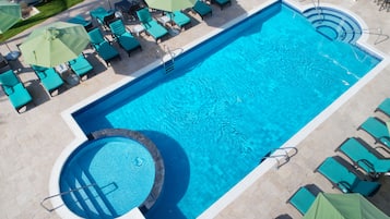 A large rectangular pool with a circular hot tub, surrounded by multiple lounge chairs and umbrellas.