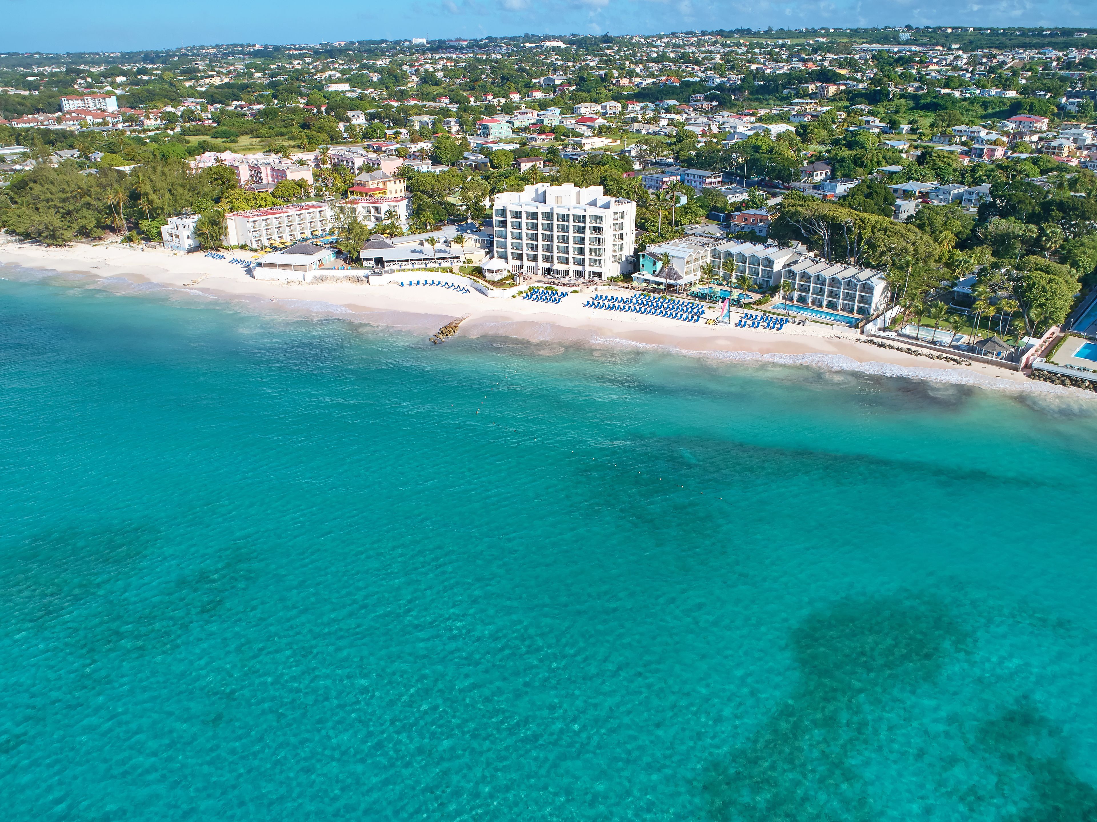 Vue aérienne d’une zone côtière avec une plage, des bâtiments d’hôtel et la végétation environnante.