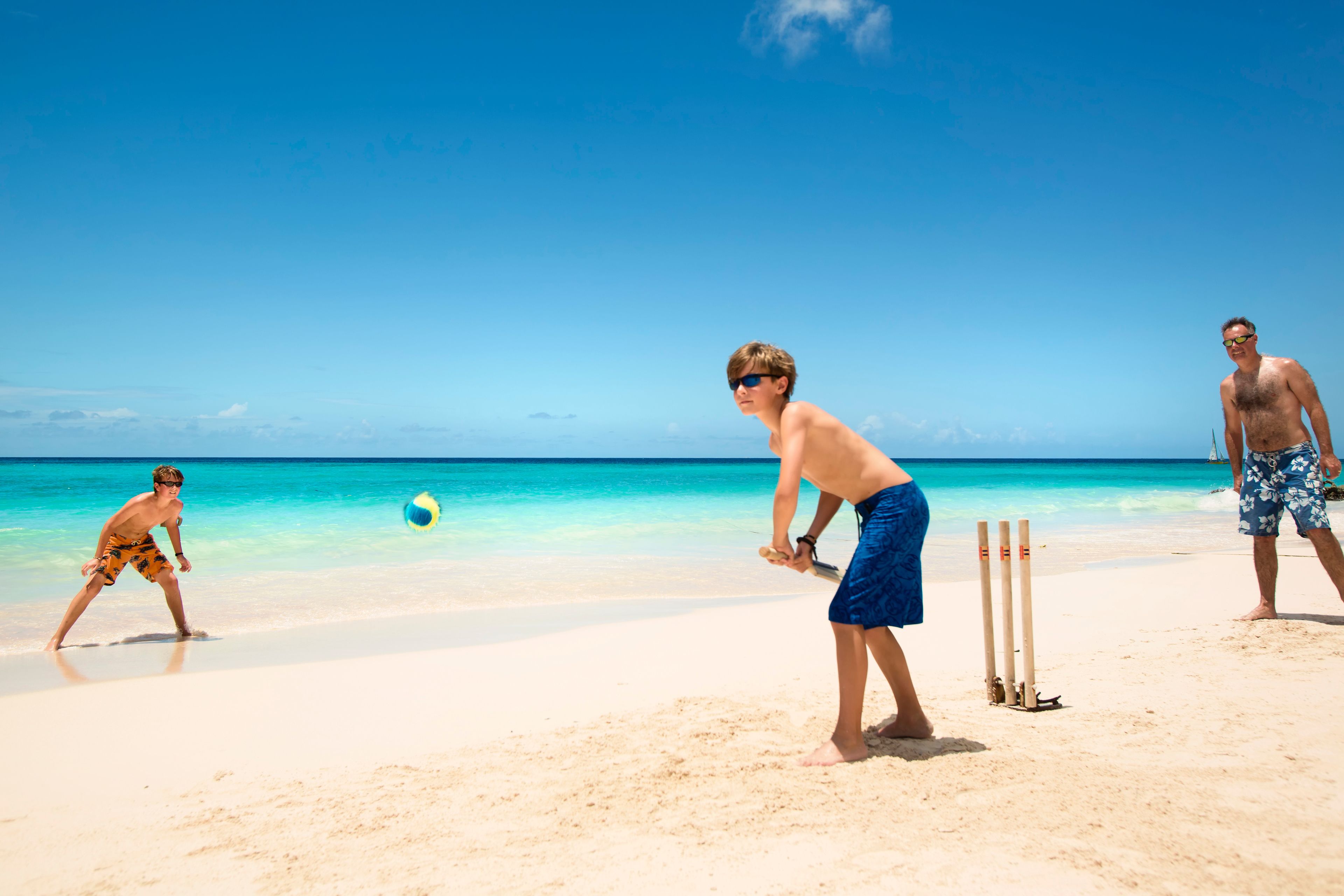Une scène de plage où trois personnes jouent au cricket.