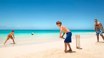 Escena de playa con tres personas jugando al cricket.