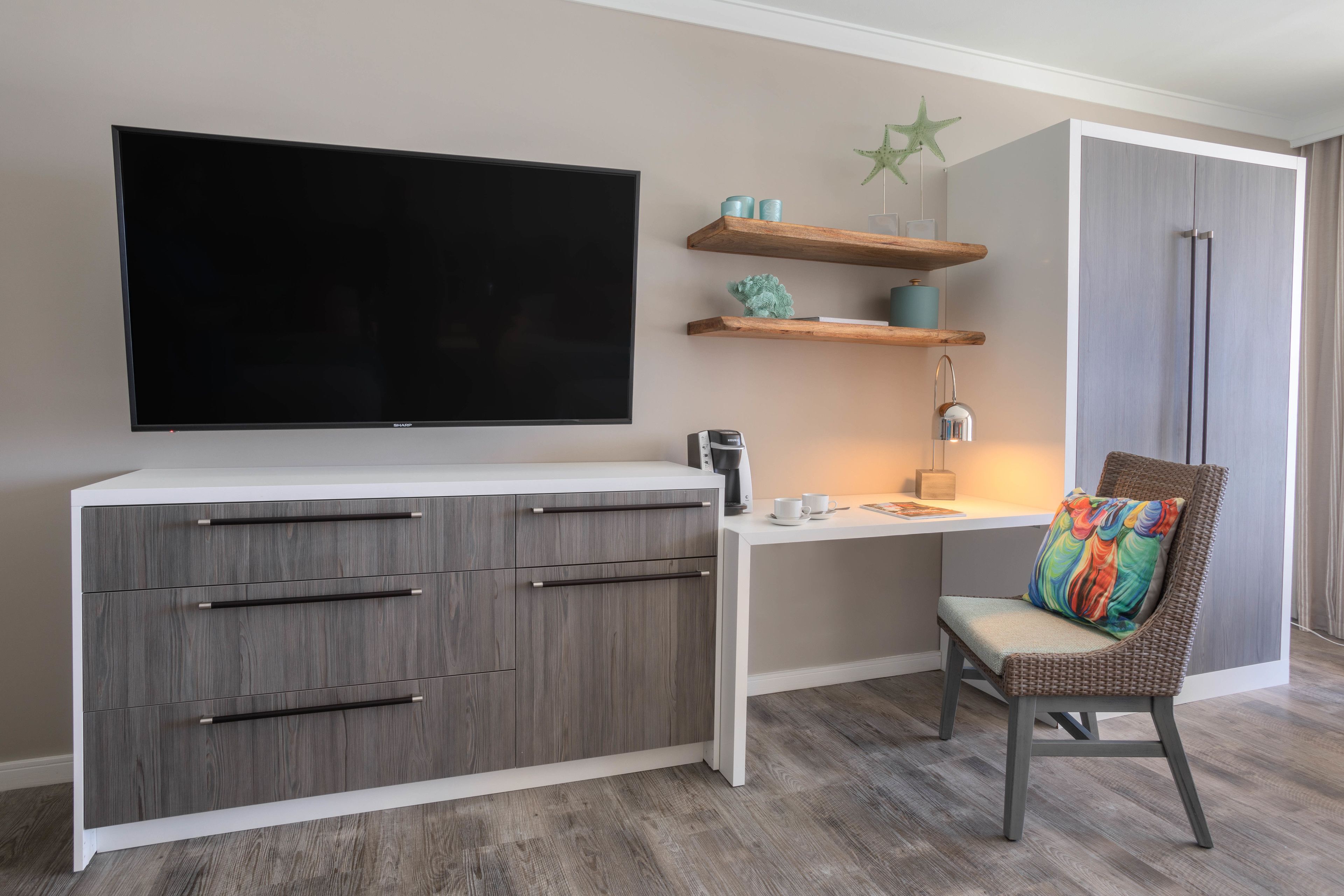 Een moderne woonkamer met een flatscreen televisie, houten kasten, een rieten stoel en een kleine tafel met een lamp.