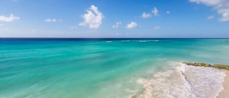 Une plage aux eaux turquoise et limpides, bordée d’un rivage sablonneux.