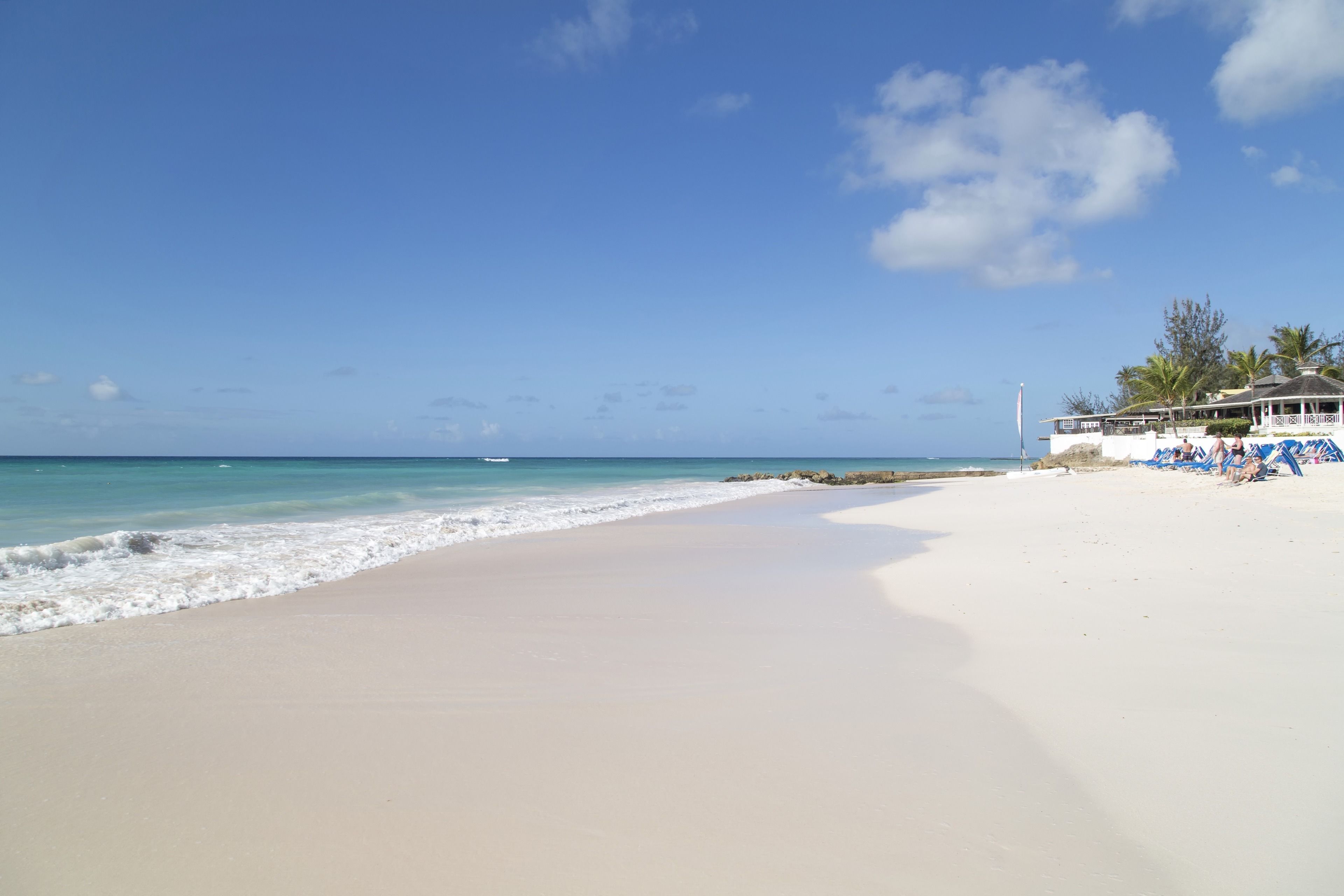 A beach with white sand, clear blue water, and a few palm trees.