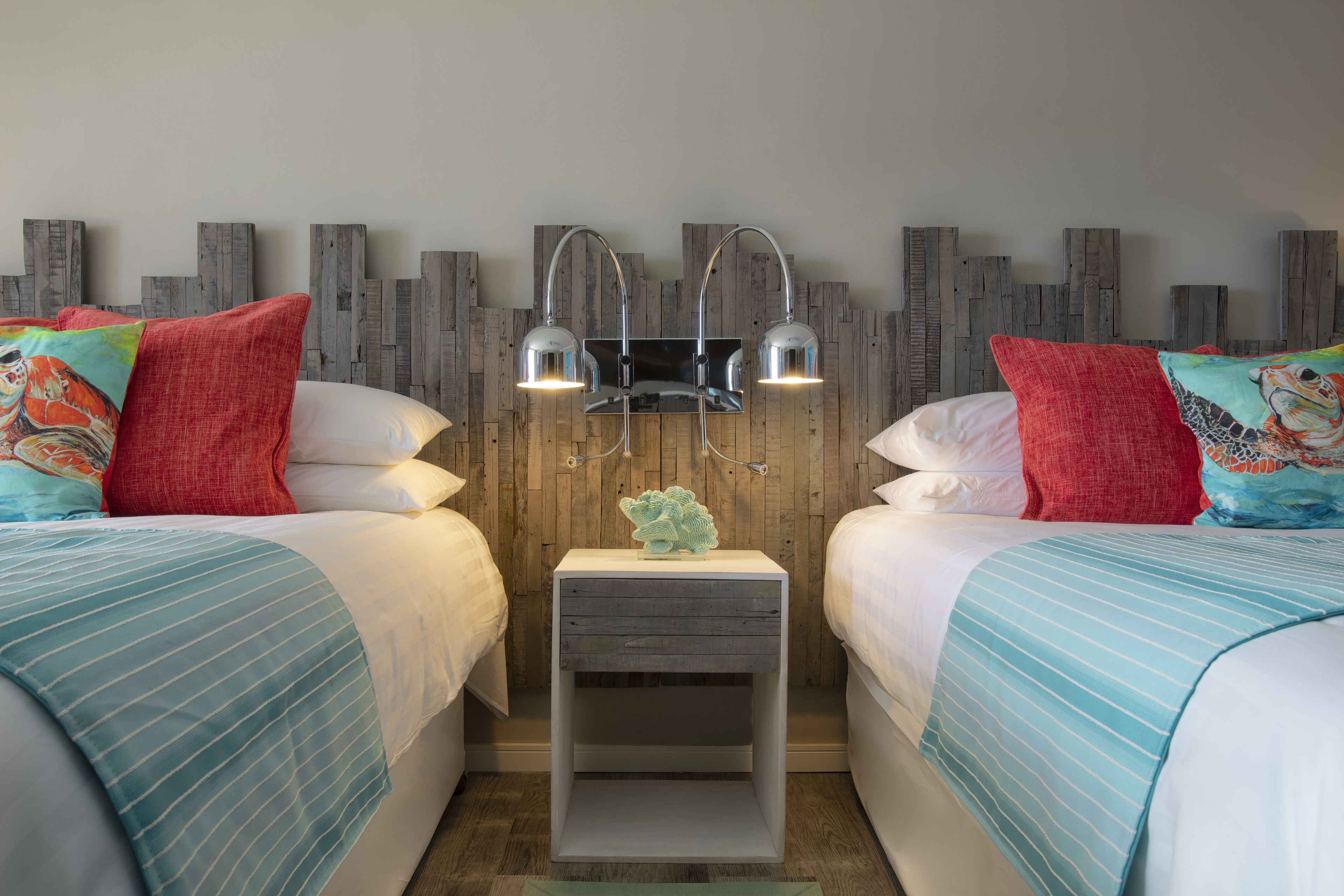 A hotel room with two beds, a nightstand with a lamp, and a decorative wall panel.