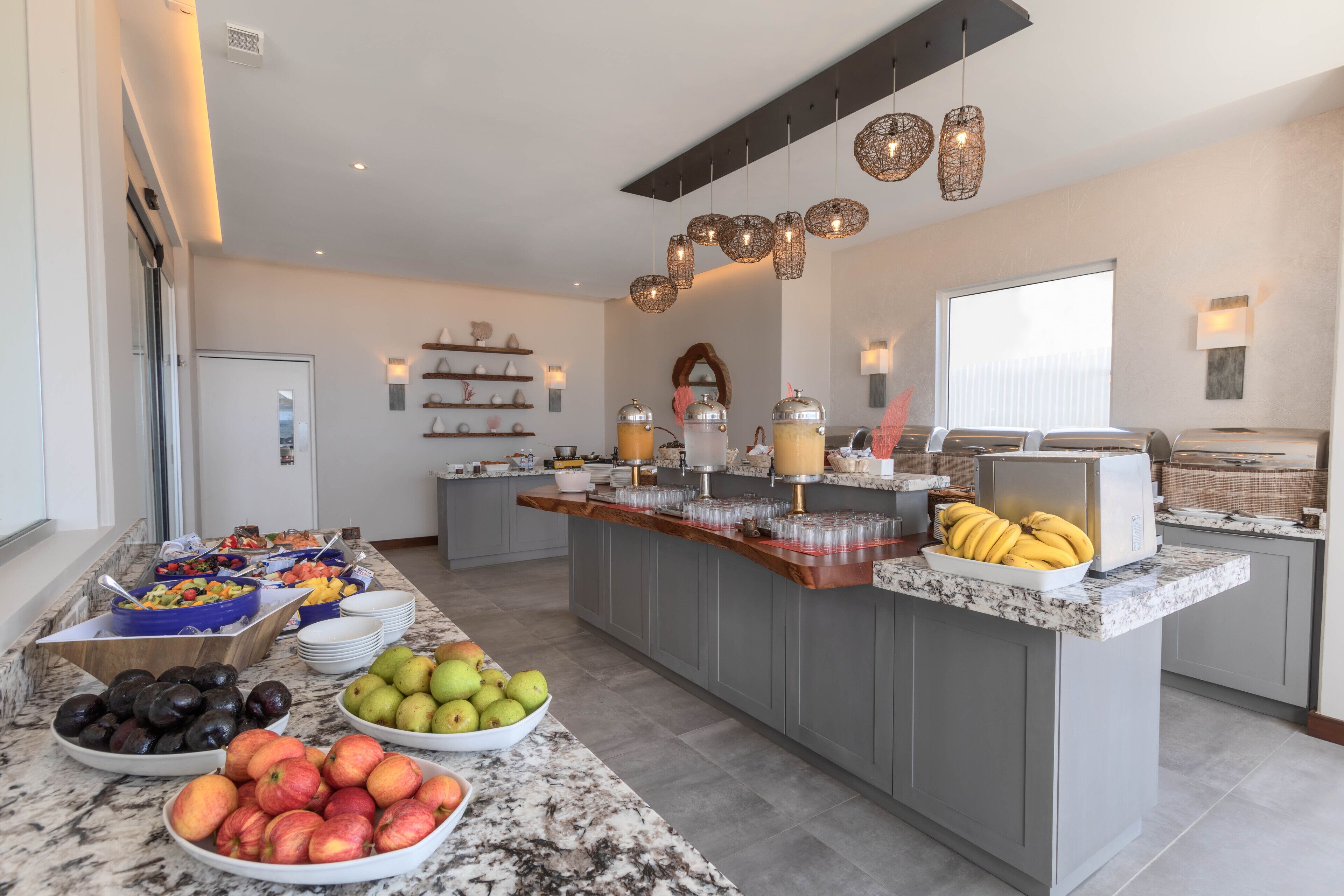 A modern kitchen with a marble countertop, a fruit bowl, and a buffet area with various food items.