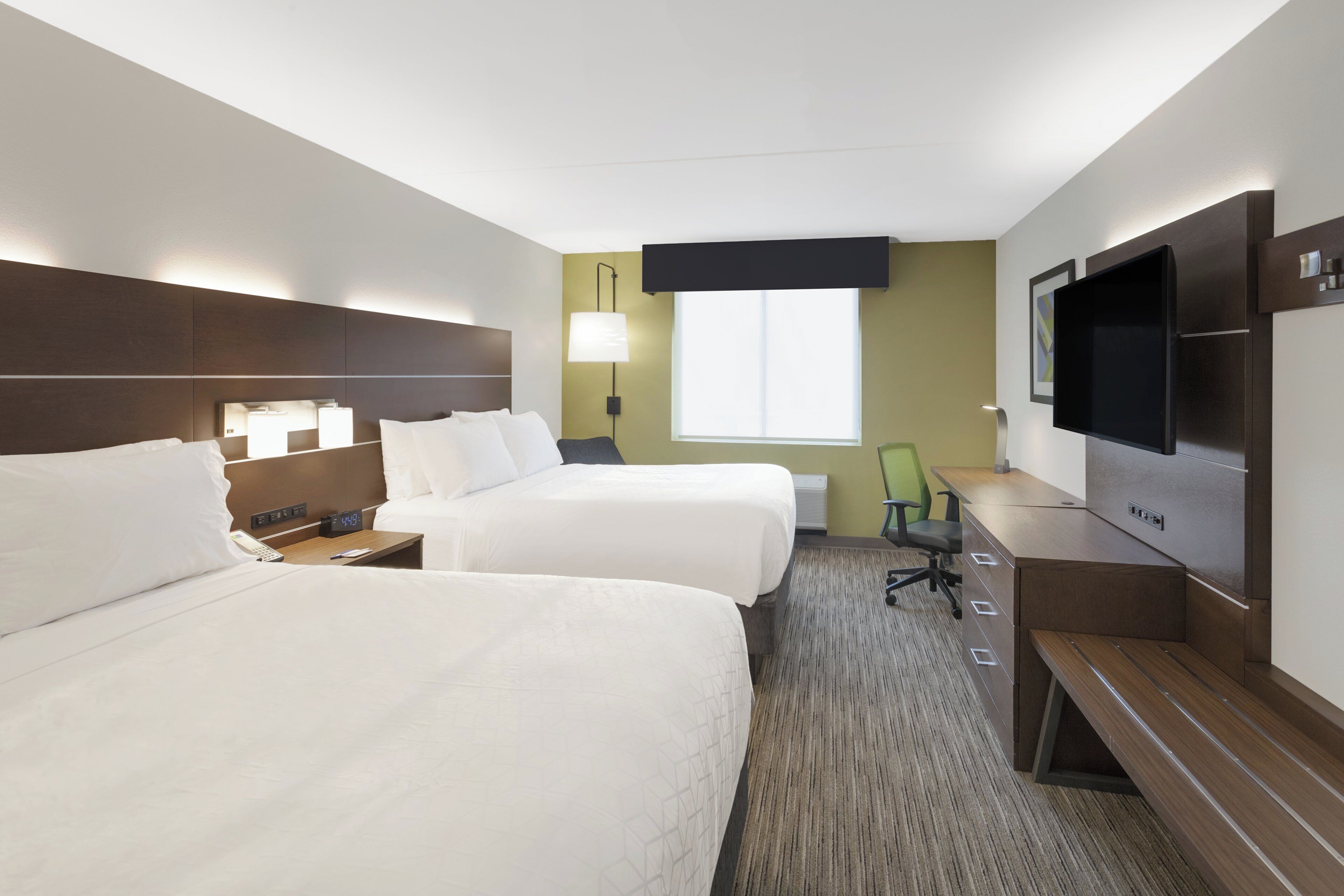A hotel room with two beds, a desk with a chair, a flat-screen TV, a lamp, and a window.